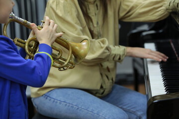 Little musician child playing the trumpet standing next to the teacher at the piano.Hand fingers...