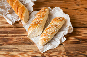 Bread baguette sprinkled sesame sesame with wrapping paper on wooden table