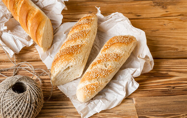 Bread baguette sprinkled sesame sesame with wrapping paper on wooden table