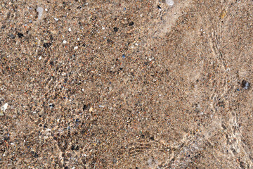 Water from the sea moving over the sand of a beach. Top down view of an idyllic holiday scene. Natural pebble ground on the bottom.