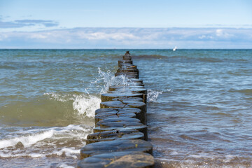 Fototapeta premium Water from the baltic sea splashing against a row of wooden planks. A wave moves towards the beach. Fresh water drops are flying through in the air.