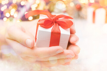 Christmas gift box with red bow in woman hands on the background of Christmas tree and snow