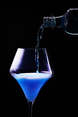 Blue drink is poured into a glass. Black background.