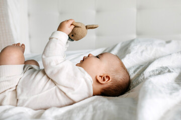 Five months old baby lying on bed, playing with a crocheted bunny toy.