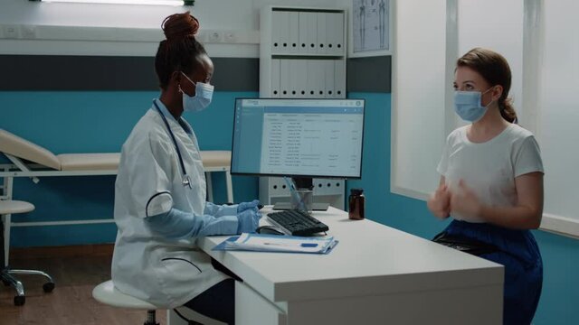 African american doctor consulting caucasian patient. Black medic talking to woman about healthcare for annual checkup visit while wearing face masks for protection against coronavirus