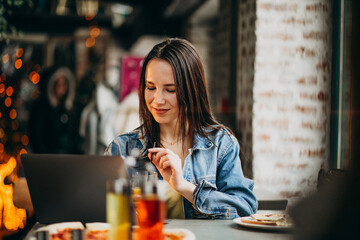 Young female student working on laptop in bar and eating pizza