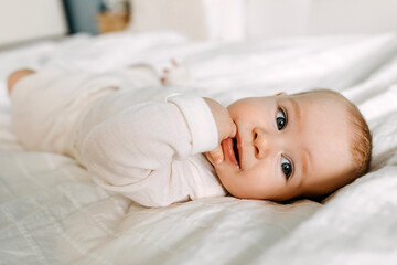 Closeup of a happy baby lying in bed, smiling, sucking fingers.