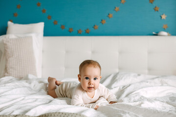 Baby lying in bed on tummy on white bed sheet, smiling, looking at camera.