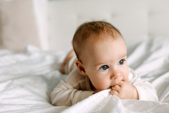 Closeup of a baby lying in bed on tummy, chewing on white bed sheet.