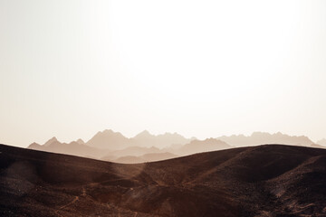 Desert landscape. Stony hills in the foreground with the silhouette of rocky mountains. Sun glare...
