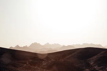 Rollo Wüstenlandschaft. Steinige Hügel im Vordergrund mit der Silhouette felsiger Berge. Sonnenblendung durch Sonnenuntergangslicht. Raum, fantastische Atmosphäre in der Sahara-Wüste © Asia Tsyhankova