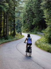 Adventurous White Caucasian Woman on a bicycle riding on a path in Green Canadian Rain Forest. Seymour Valley Trailway in North Vancouver, British Columbia, Canada.