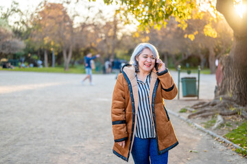 Portrait of a woman with gray hair using the phone at the park at sunset