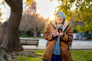 Portrait of a woman with gray hair using the phone at the park at sunset
