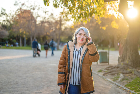 Portrait of a woman with gray hair using the phone at the park at sunset