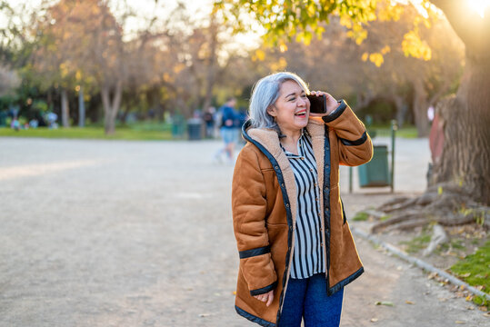 Portrait of a woman with gray hair using the phone at the park at sunset
