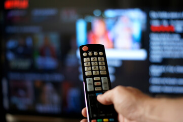 Male hand holding tv remote control. The focus of the photo is on the remote control. The background and hand are blurred