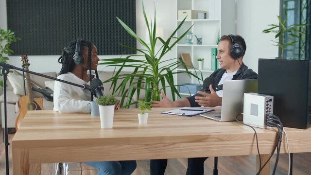 A Male Presenter Communicates with a Guest, an African American, During a Radio Broadcast at a Table in a Recording Studio, Broadcasts a Live Radio Interview With Spbd. Male Host Sharing Content.