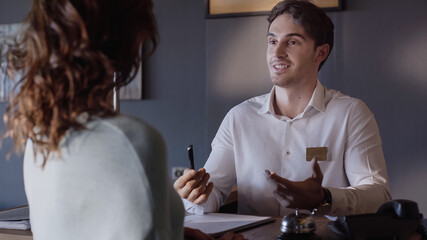 smiling hotel receptionist talking with blurred woman at hotel counter.