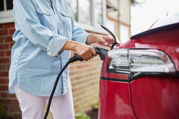 Close Up Of Woman Attaching Charging Cable To Environmentally Friendly Zero Emission Electric Car...