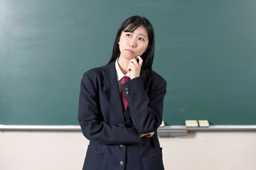 黒板の前で悩む制服を着た笑顔の女子学生
