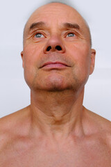 Obraz premium close-up face of elderly bald tanned man 60 years old with naked torso looking, smiling, wrinkles and age spots, aging problems, concept of male age, midlife crisis