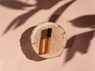Perfume sample with yellow liquid on wooden tray lying on beige background with shadows above. Luxury and natural cosmetics presentation. Tester on woodcut in the sunlight. Shades and lights. Top view