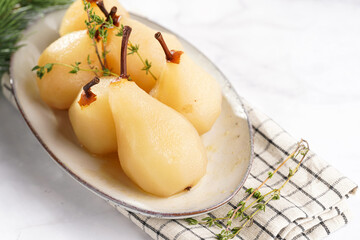 Peeled poached pears on a white oval plate on a checkered linen cloth and a christmas fair-tree branch on a white table surface