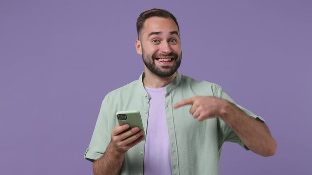Excited surprised joyful young bearded man 20swears mint shirt hold use mobile cell phone typing say wow yes just found out great big win news isolated on plain light purple background studio portrait