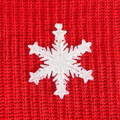 white shiny figurine of a snowflake on a red knitted background..