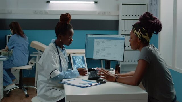 African american patient and doctor looking at radiography on tablet, talking about healthcare diagnosis at annual checkup visit. Black medic holding x ray scan for examination with woman