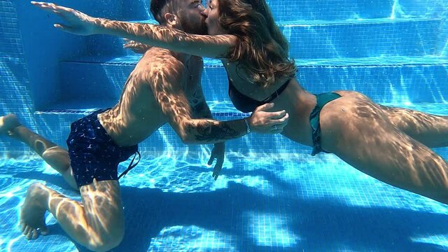 Cheerful romantic couple swimming in pool in summer time