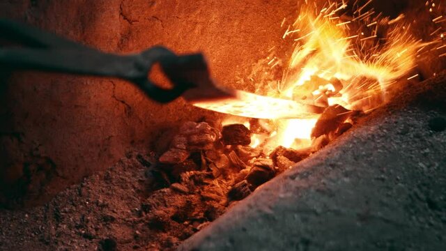 Red hot metal piece taken out of a smithy furnace fire, slow motion