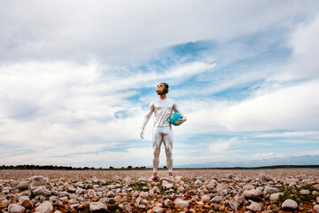Male with geometric monkey mask holding globe in nature