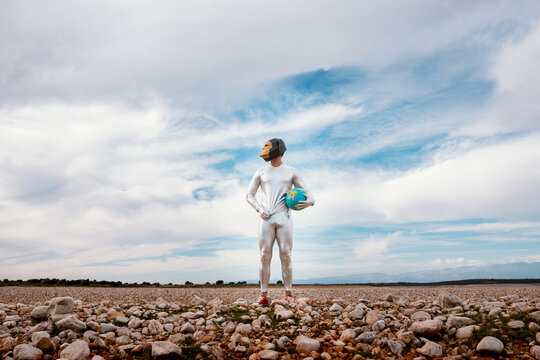 Male with geometric monkey mask holding globe in nature