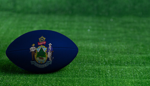 American football ball  with Maine flag on green grass background, close up