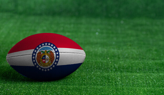 American football ball  with Missouri flag on green grass background, close up