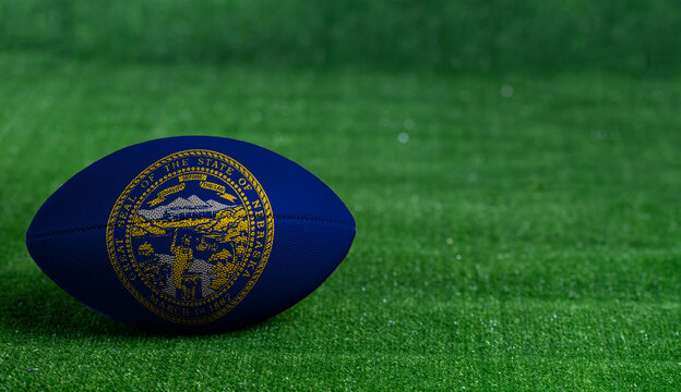 American Football Ball  With Nebraska Flag On Green Grass Background, Close Up