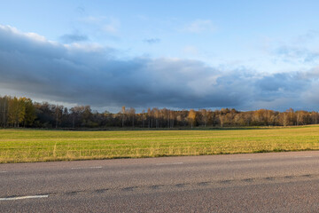 Beautiful autumn nature landscape view. Highway between green fields on blue sky background. Sweden. 