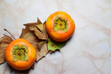 Persimmon, autumn fruit, natural leaves on marble background. Copy space.