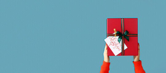 Young woman holding Christmas gift on color background with space for text