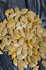 Pumpkin seeds are scattered on the surface of black pine boards. Close-up shot.