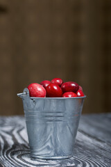 A metal bucket filled with ripe red cranberries. Autumn berries. On black pine boards. Close-up shot.