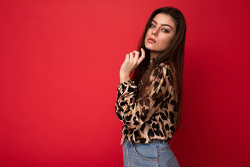 Image of a beautiful young brunette woman dressed in animal printed blouse posing isolated over red background with copy space