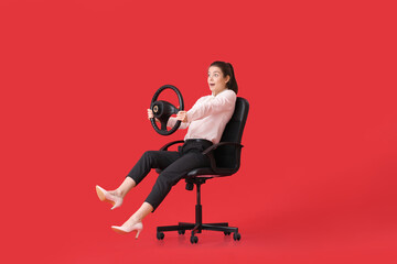 Surprised young businesswoman with steering wheel sitting in chair on color background