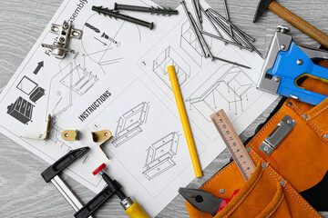 Furniture assembling instructions and scattered tools on grey wooden background, closeup