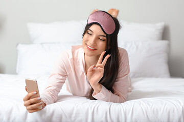 Pretty young woman taking selfie and showing victory gesture in bedroom