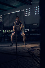 Athlete man training with rope, exercising with crossed combat ropes, training intensely indoors, in modern gym. Sports motivation concept. Copy space