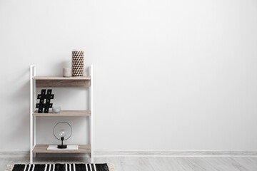 Stylish shelf unit with decor near light wall