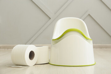 Potty and toilet paper rolls on floor near grey wall